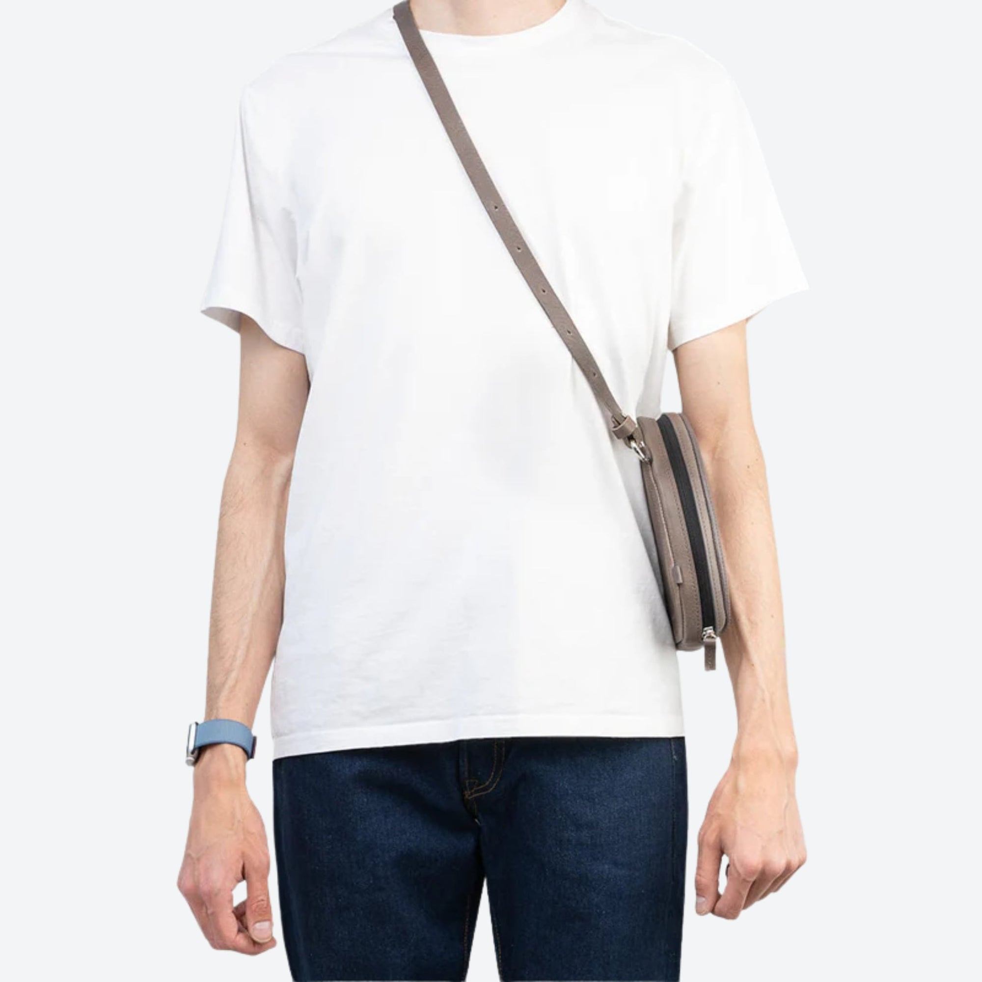 Person wearing a white t-shirt and dark jeans with a brown crossbody bag on a white background