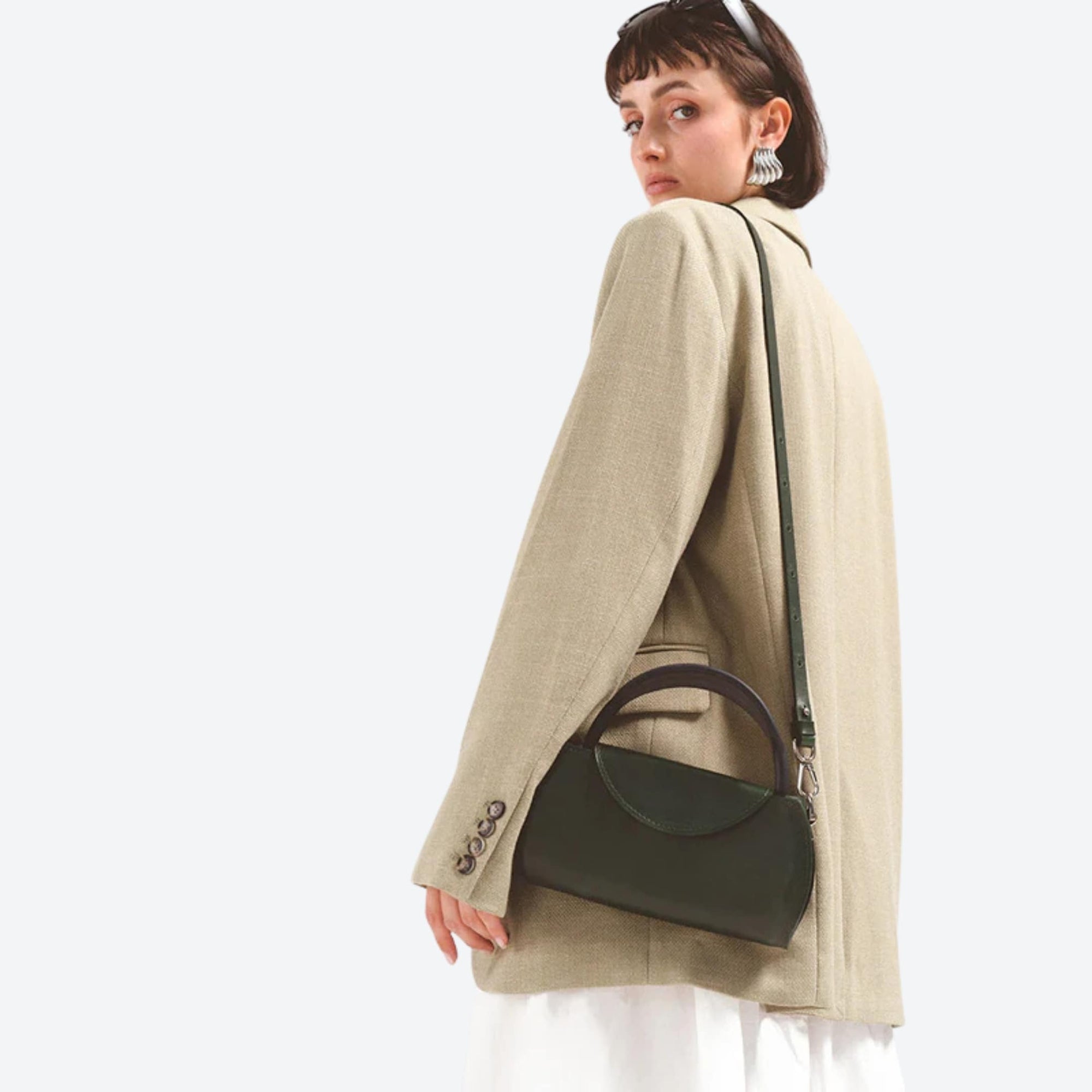 Woman wearing a beige coat with a green handbag on a white background